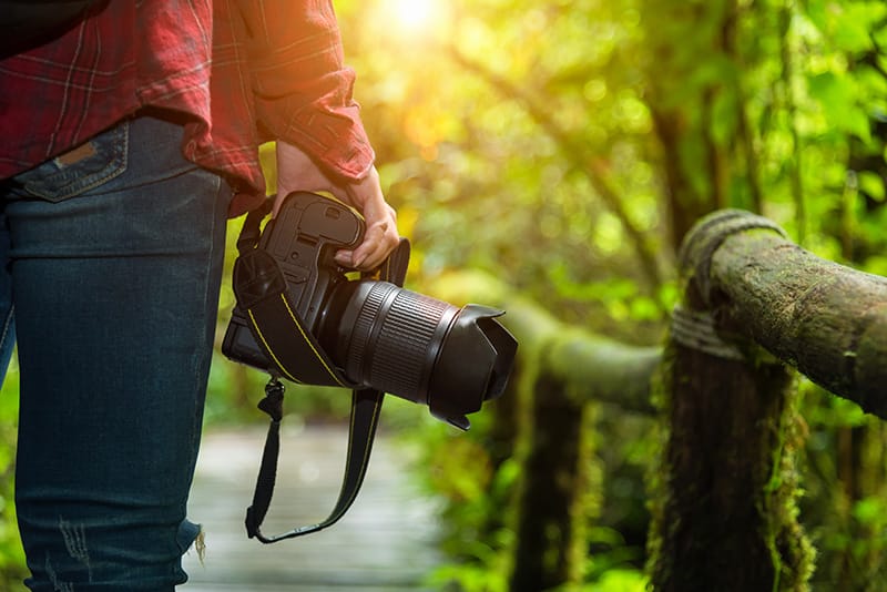 Detalle de cámara profesional de fotografía en manos de una mujer en parque 