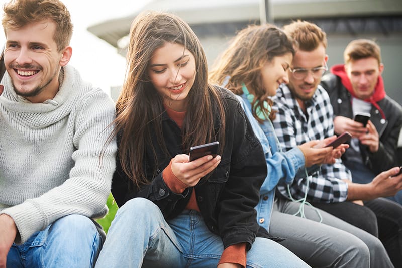 Personas de Generación Z sentados en un muro mirando sus celulares y riendo