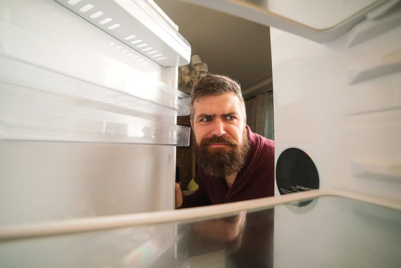 Hombre mira interior de refrigerador con cara de desconfiado